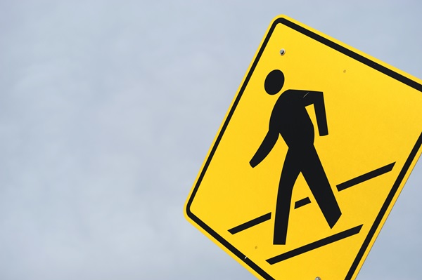 A yellow pedestrian crossing sign against a blue sky background.